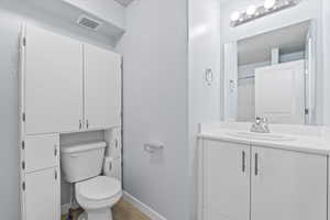 Bathroom with toilet, baseboards, visible vents, vanity, and wood finished floors