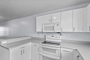 Kitchen with a peninsula, white appliances, light countertops, and white cabinets