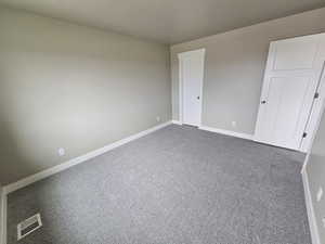 Empty room with baseboards, dark colored carpet, and visible vents