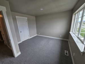 Unfurnished bedroom featuring baseboards, dark carpet, and visible vents