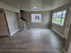 Unfurnished living room with a textured ceiling, stairs, visible vents, and wood finished floors