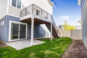 Rear view of house with fence, stairs, stucco siding, a lawn, and a patio