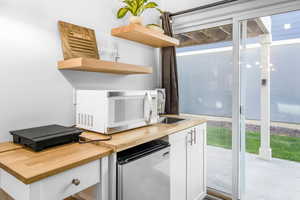 Interior space with open shelves, refrigerator, wooden counters, white microwave, and white cabinetry