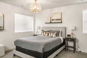 Carpeted bedroom featuring baseboards, visible vents, multiple windows, and a chandelier