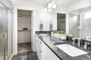 Bathroom with wood finished floors, a sink, a walk in closet, and a stall shower