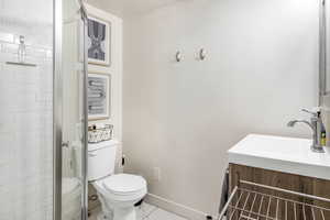Bathroom featuring walk in shower, vanity, toilet, marble finish floor, and baseboards