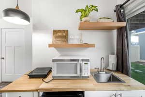 Interior space with a sink, open shelves, wood counters, and white microwave
