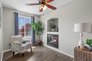 Living area with a ceiling fan, wood finished floors, baseboards, and a glass covered fireplace