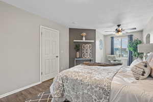 Bedroom with a textured ceiling, dark wood-style flooring, baseboards, and ceiling fan