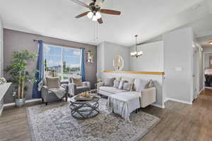 Living area with vaulted ceiling, ceiling fan with notable chandelier, baseboards, and wood finished floors