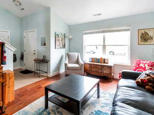 Living room with vaulted ceiling, wood finished floors, visible vents, and stairs