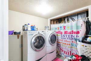 Laundry room with laundry area, a textured ceiling, and separate washer and dryer