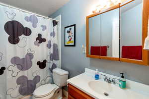 Bathroom with toilet, shower / tub combo with curtain, vanity, and a textured ceiling