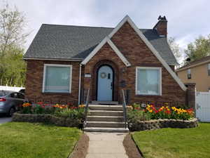 Tudor-style house with brick siding, roof with shingles, a chimney, and a front yard