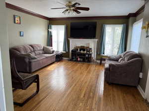 Living area with a ceiling fan, a textured ceiling, baseboards, crown molding, and wood finished floors