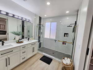 Bathroom featuring a sink, a stall shower, ensuite bath, and wood finished floors