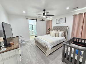 Bedroom with light colored carpet, visible vents, a barn door, recessed lighting, and ensuite bath