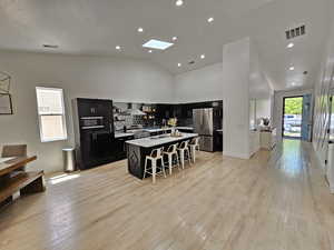 Kitchen featuring visible vents, a kitchen breakfast bar, wall chimney exhaust hood, dark cabinetry, and stainless steel appliances