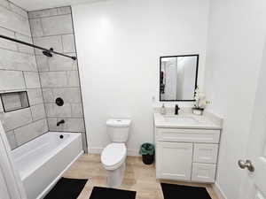 Full bathroom with vanity, wood finished floors, toilet, baseboards, and shower / tub combination