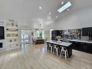 Kitchen featuring visible vents, a kitchen breakfast bar, an island with sink, wall chimney range hood, and dark cabinetry