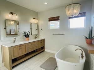 Full bathroom with double vanity, a sink, a chandelier, and a soaking tub