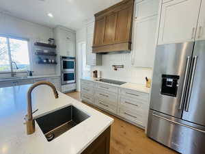 Kitchen with a sink, custom exhaust hood, stainless steel appliances, and backsplash