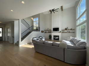 Living room with a large fireplace, wood finished floors, stairway, a high ceiling, and recessed lighting
