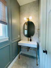 Bathroom with wallpapered walls, a sink, tile patterned floors, and baseboards