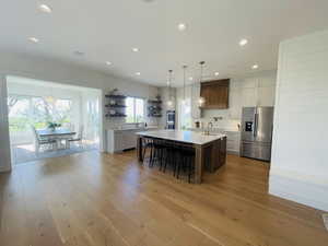 Kitchen featuring open shelves, decorative backsplash, a kitchen bar, light countertops, and appliances with stainless steel finishes