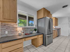 Kitchen featuring built in desk, light tile patterned floors, stainless steel appliances, and backsplash