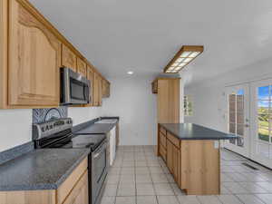 Kitchen with dark countertops, appliances with stainless steel finishes, light tile patterned floors, and a healthy amount of sunlight