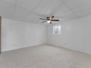 Carpeted spare room featuring a drop ceiling and ceiling fan