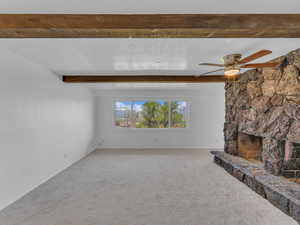 Unfurnished living room with a ceiling fan, beamed ceiling, and carpet floors