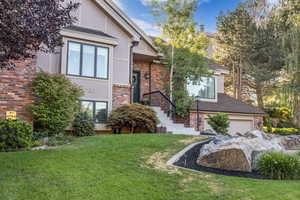 View of front of property with a front lawn, stucco siding, a garage, a shingled roof, and brick siding
