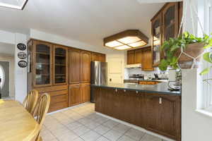 Kitchen with a peninsula, brown cabinets, dark countertops, under cabinet range hood, and appliances with stainless steel finishes