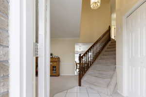 Stairs with baseboards, carpet flooring, tile patterned floors, a chandelier, and crown molding