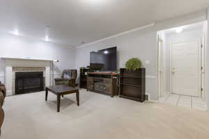 Living area featuring baseboards, a glass covered fireplace, visible vents, crown molding, and light carpet