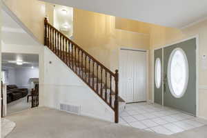 Carpeted entrance foyer featuring ornamental molding, tile patterned flooring, stairway, and visible vents