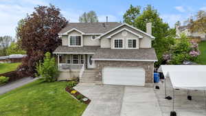Traditional-style home featuring a porch, a garage, roof with shingles, concrete driveway, and a chimney