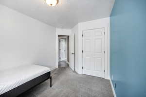 Carpeted bedroom featuring baseboards, a closet, and a textured ceiling