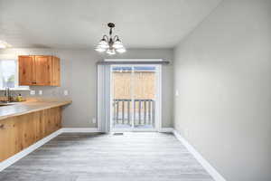 Kitchen featuring a textured ceiling, plenty of natural light, baseboards, light wood finished floors, and an inviting chandelier