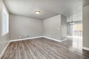 Empty room with an inviting chandelier, a textured ceiling, and wood finished floors