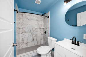 Bathroom featuring vanity, toilet, tiled shower, and visible vents