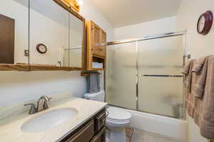Full bath with toilet, combined bath / shower with glass door, vanity, and tile patterned floors