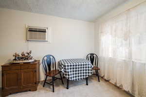 Dining area featuring light colored carpet, a textured ceiling, and a wall unit AC