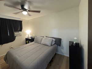 Bedroom with wood finished floors, a ceiling fan, and cooling unit