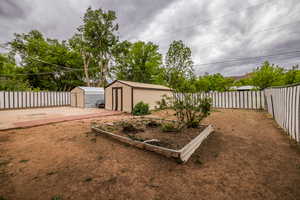 Fenced backyard with an outdoor structure, a storage shed, and a vegetable garden