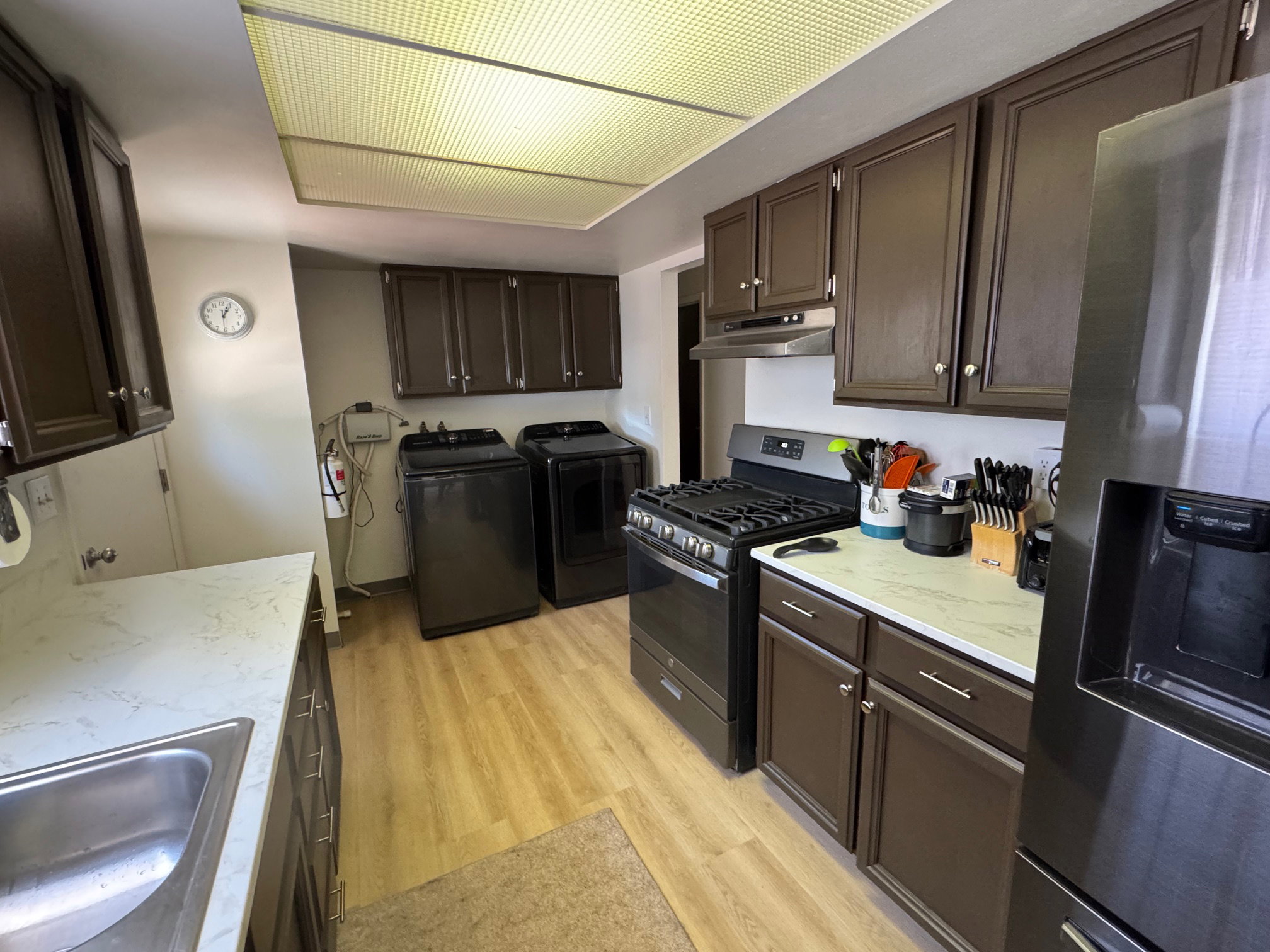 Kitchen featuring stainless steel fridge, independent washer and dryer, range with gas stovetop, under cabinet range hood, and light wood-style flooring
