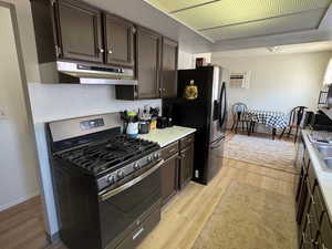 Kitchen featuring range with gas cooktop, under cabinet range hood, black fridge, and dark brown cabinetry