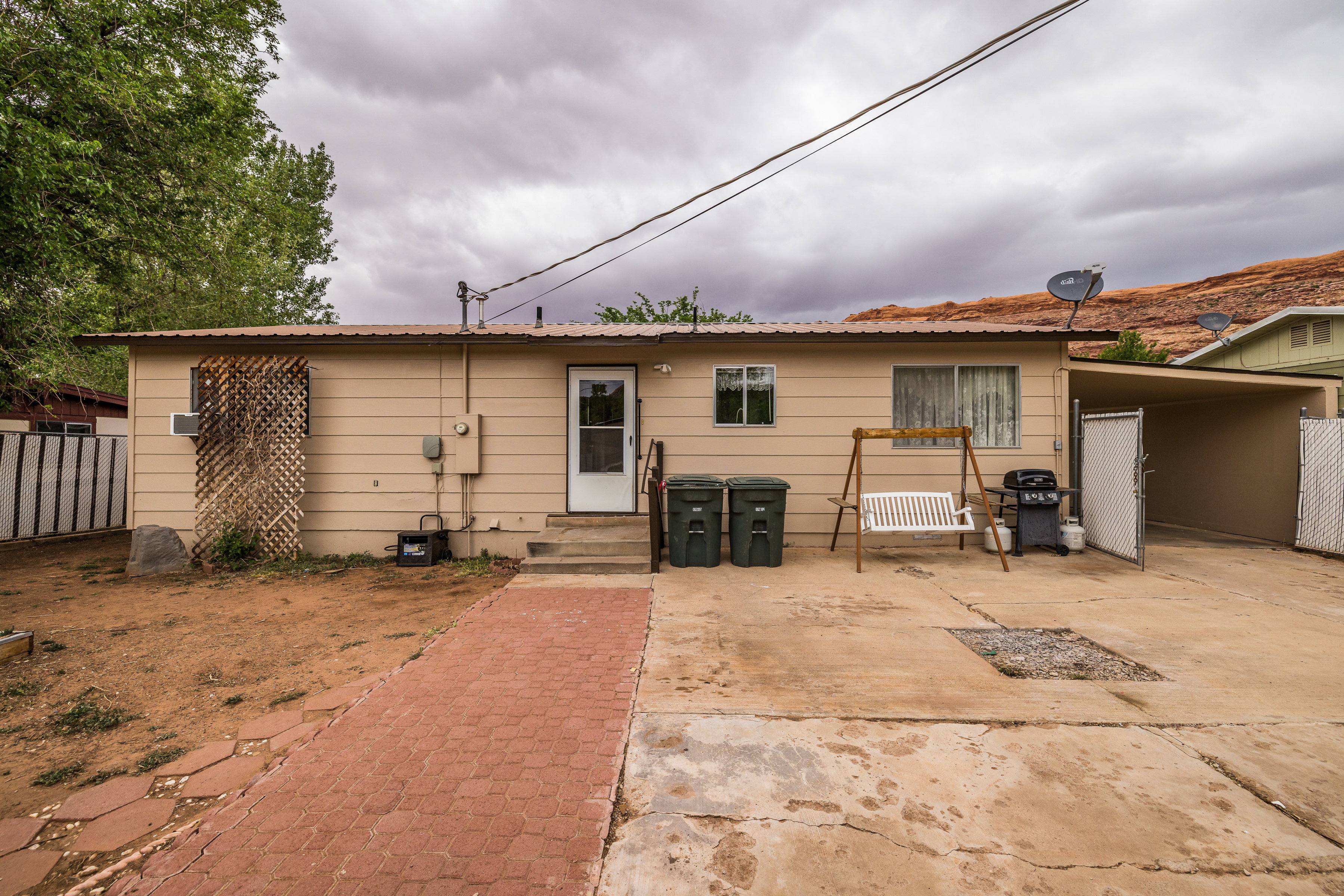 Rear view of property featuring new entry doors steps, an attached carport, fence, and metal roof